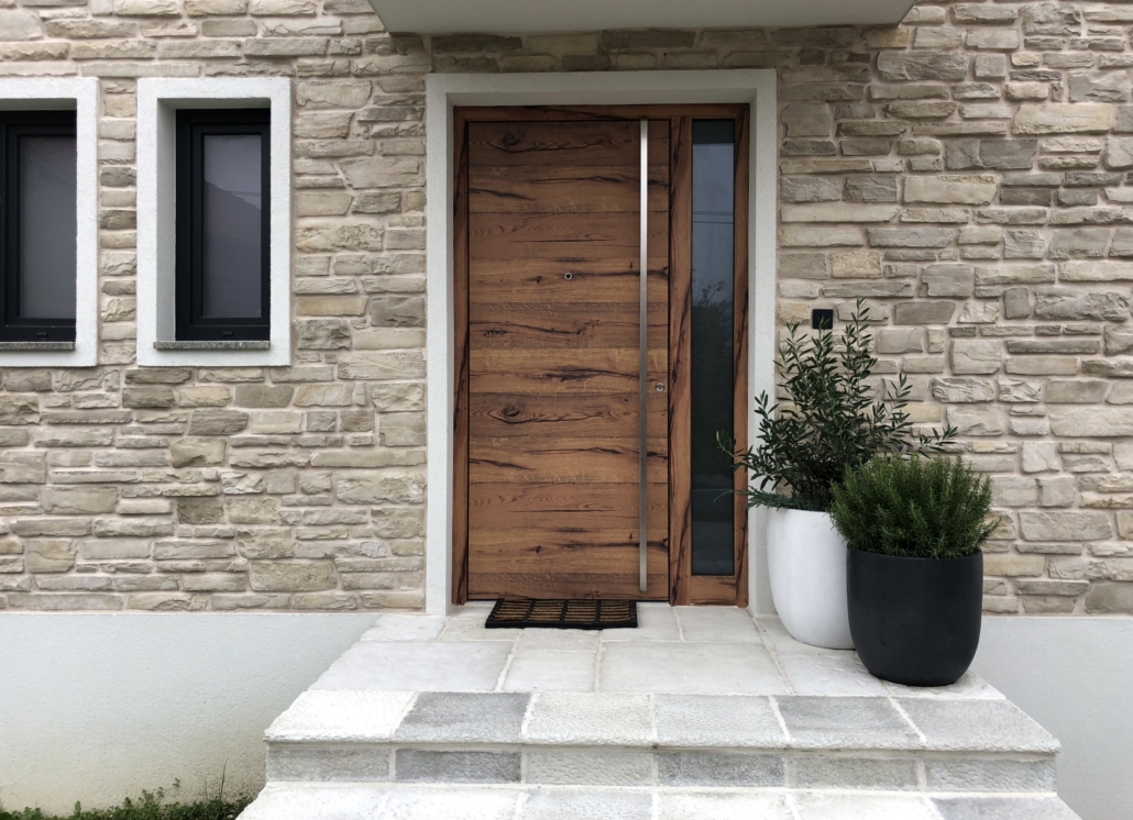 Front door in a wood finish with a long stainless steel handle and a sidelight