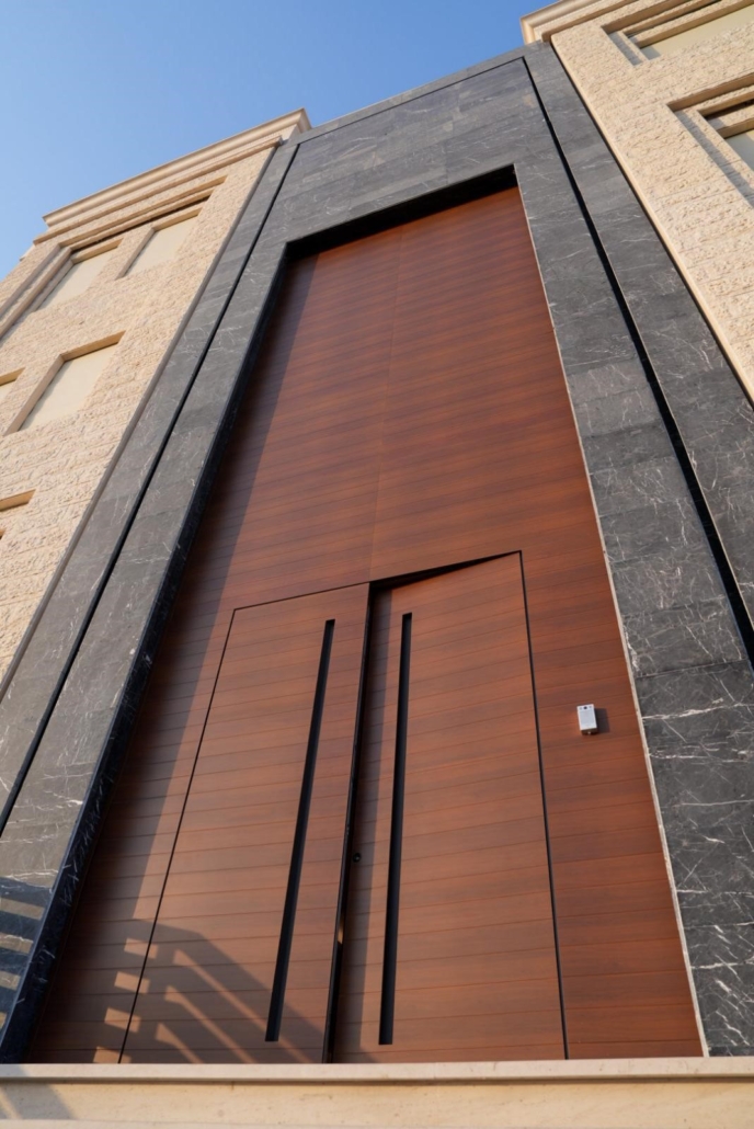 Double front door in a wood finish with a large overdoor panel and recessed handles